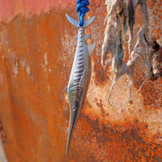 Metallic fish-shaped object hanging on a rusty surface