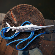Metallic fish-shaped object with blue rope on a wooden surface