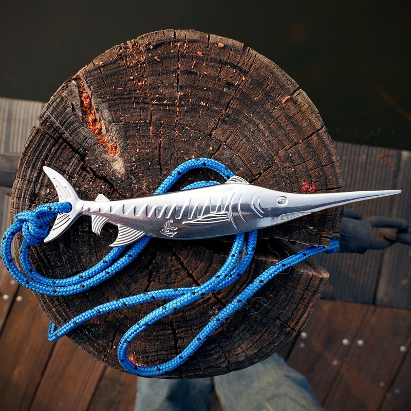 Metallic fish-shaped object with blue rope on a wooden surface